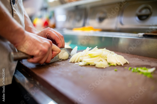 A skilled chef meticulously slices onions on a wooden cutting board in a well-equipped kitchen, showcasing precision and culinary artistry
