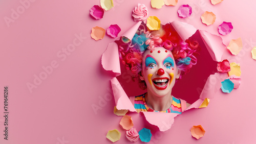 A colourful clown with blue hair smiling through a torn pink paper background, portraying humor