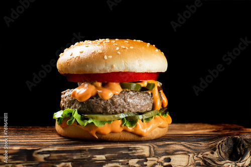 cheeseburger with a cutlet on a wooden board and a black background with a bright orange sauce