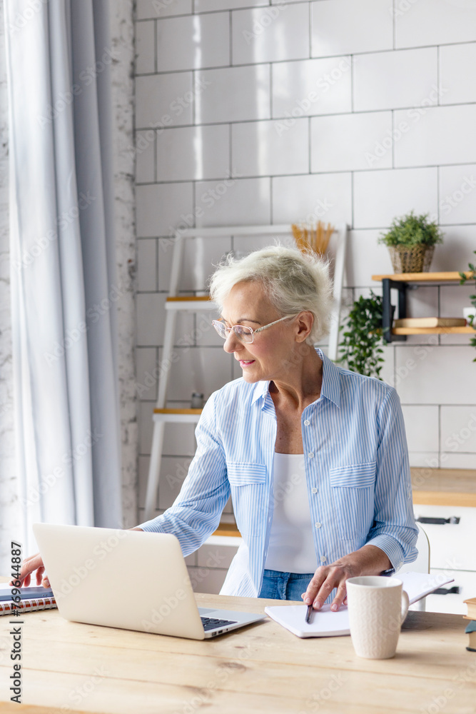 beautiful elderly senior woman in cosy kitchen works on laptop and speaking by phone, beautiful gray haired woman works online, pays bills, studies and communicates, concept of active old age beautiful elderly senior woman in cosy kitchen works on laptop and speaking by phone, beautiful gray haired woman works online, pays bills, studies and communicates, concept of active old age