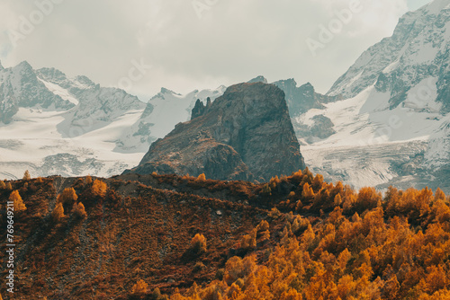 High mountain among the autumn forest, snow-capped mountains in the background