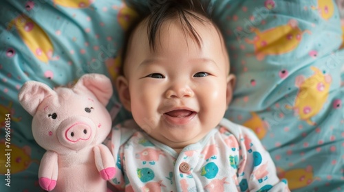 A joyful baby with a pink stuffed pig both resting on a colorful playful blanket.