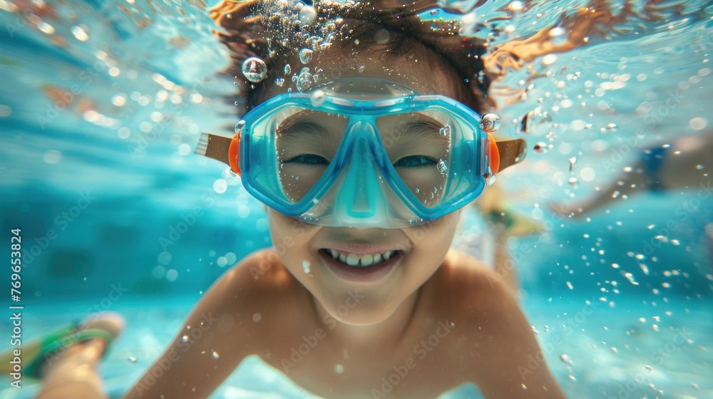 A young child wearing blue goggles smiling underwater with bubbles around them enjoying a swim in a pool.