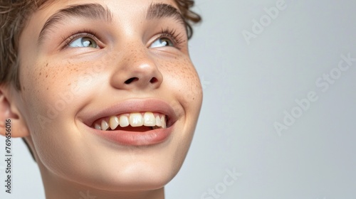 A close-up of a young person with freckles smiling with their eyes closed against a white background. © iuricazac