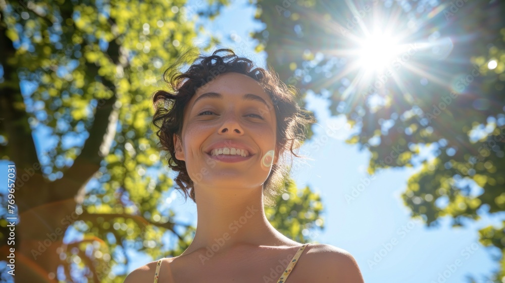 Smiling woman with curly hair looking up at the sun surrounded by green leaves and blue sky. Smiling woman with curly hair looking up at the sun surrounded by green leaves and blue sky.