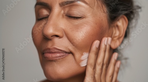 Woman with closed eyes applying cream to her face showcasing a moment of self-care and relaxation.