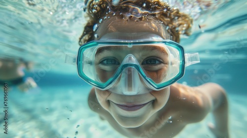 A young child with curly hair wearing blue goggles smiling underwater.