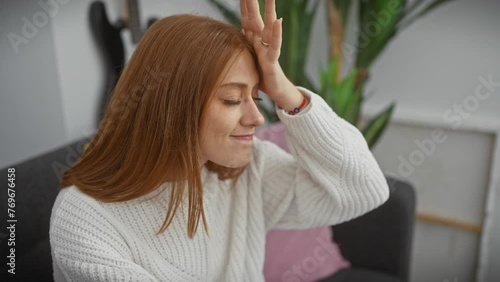Oops! young redhead woman, surprised at home wearing sweater, hand on head remembering forgotten mistake - a foolish blunder hitting her memory