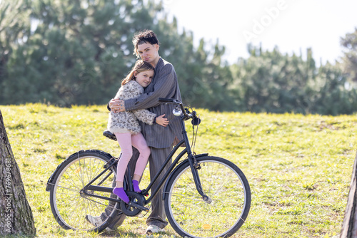 A woman and a little girl - her daughter - are hugging each other while sitting on a bicycle