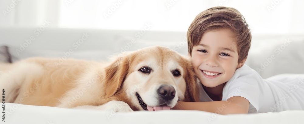 A young boy is lying on a bed with his golden retriever dog. The boy is smiling and looking at the camera. The dog is lying next to him with its head on the boys arm.