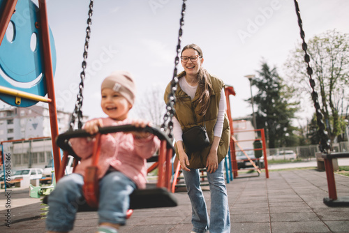 Mother and daughter playing on the playground swing
