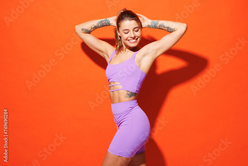 Side profile view young fitness trainer instructor sporty woman sportsman wear purple top clothes spend time in home gym look camera isolated on plain orange background. Workout sport fit abs concept.
