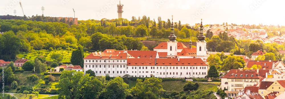 The historic Strahov Monastery basks in the warm glow of the setting sun, with verdant trees surrounding the majestic architecture in Prague, Czechia