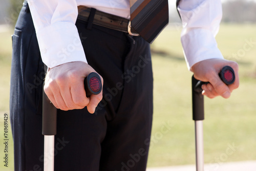 A man in formal wear, with a blazer and suit trousers, is using crutches