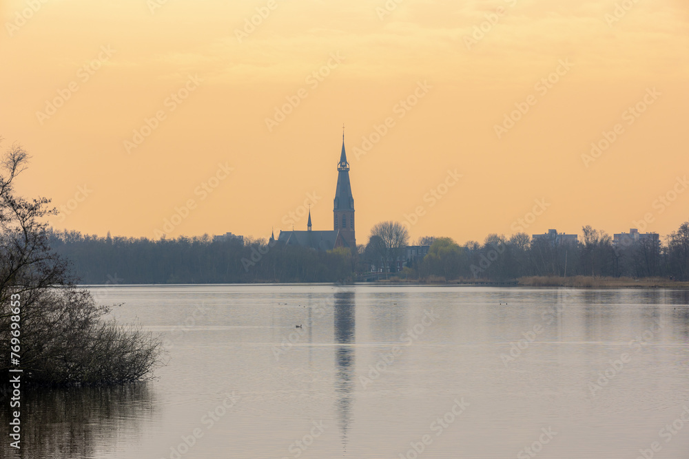 Landscape view of De Poel lake, Golden sky in the morning or evening during sunrise or sunset, Reflection of Bovenkerk (Church) on water, Amsterdamse Bos, Park in Amstelveen and Amsterdam, Netherlands