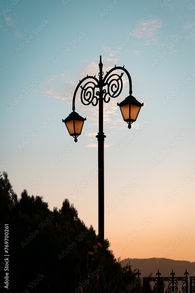 Picturesque landscape featuring a large street light standing tall with trees in the background Picturesque landscape featuring a large street light standing tall with trees in the background