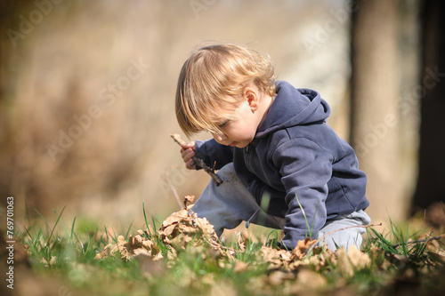 Toddlers autumn adventure. Curious kid crouches among fallen leaves, discovering the wonders of nature. Child playing outdoors