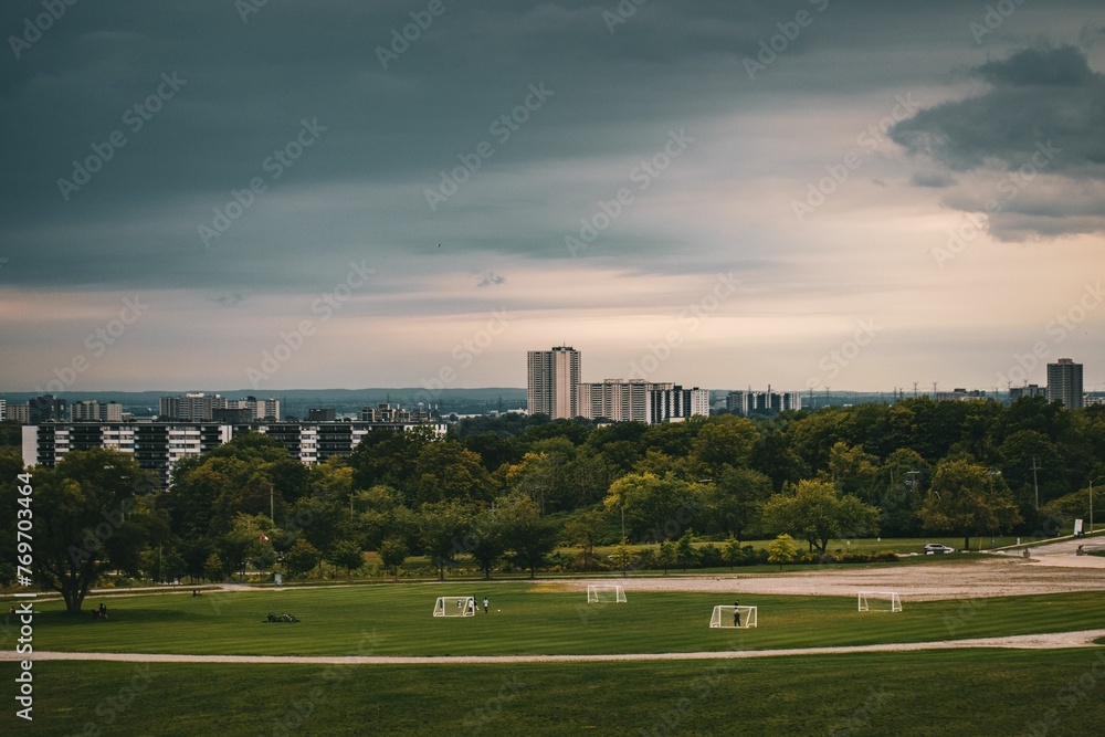 View of a soccer field in the foreground, with a cityscape and a dark, cloudy sky in the background View of a soccer field in the foreground, with a cityscape and a dark, cloudy sky in the background