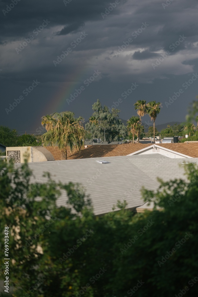 Dark and moody sky with rainbow above the rooftops and palm trees Dark and moody sky with rainbow above the rooftops and palm trees