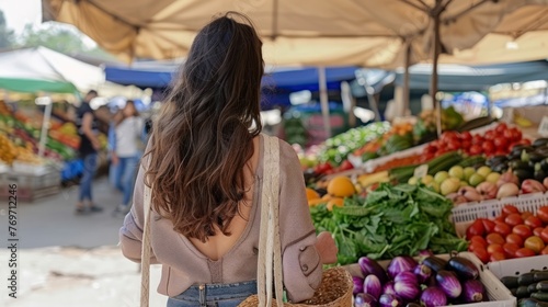 Young woman at farmers market with an eco friendly straw bag full of healthy produce. Conscious shopping for organic fruits and vegetables
