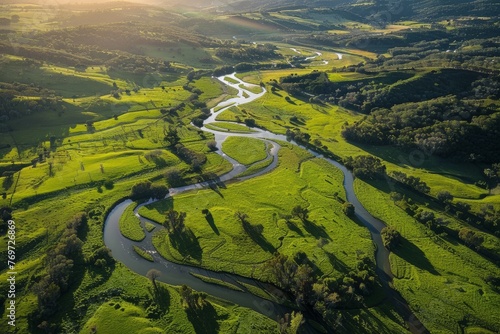 A river winds its way through a vibrant green countryside, illuminated by sunlight filtering through the trees