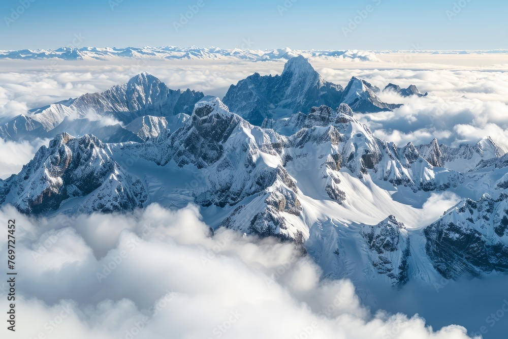Snow blankets jagged peaks of a mountain range as clouds hang low in this high-altitude aerial view