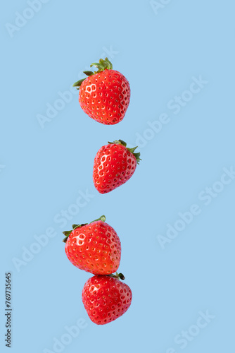 Levitation of ripe red strawberries. Flying a few strawberries with green leaves on a blue background. Summer berry © Alena