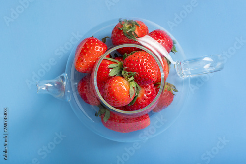 Glass transparent teapot full of red ripe strawberries on a blue background. Summer is a healthy drink. Summer berry tea © Alena