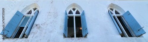 Obraz na płótnie Three open windows with blue shutters of a church.