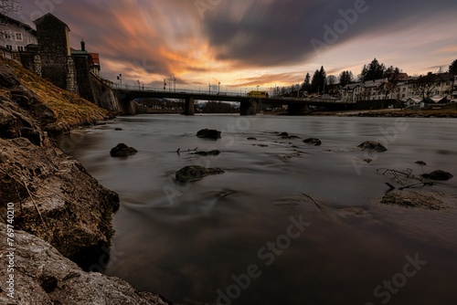 Cloudy sky at sunset over a river with a bridge, creating a somber atmosphere