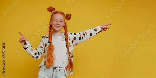 Portrait of a happy redhair girl, pointing fingers to side, on yellow background photo