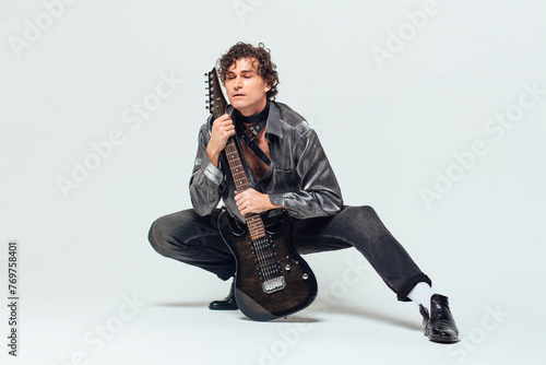 Tall attractive man holding electro guitar standing on the white background