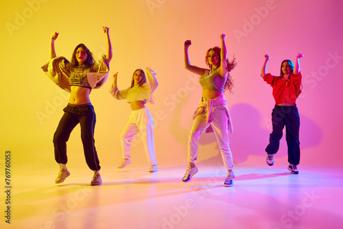 Stylish young women in sport style casual clothe sin motion, dancing hip hop, contemp against gradient background in neon light. Concept of youth, street dance, contemporary dance, modern, dynamics