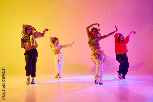 Dynamic image of young people, female dancers in motion dancing modern style dance against gradient background in neon light. Concept of youth, street dance, contemporary dance, modern, dynamics