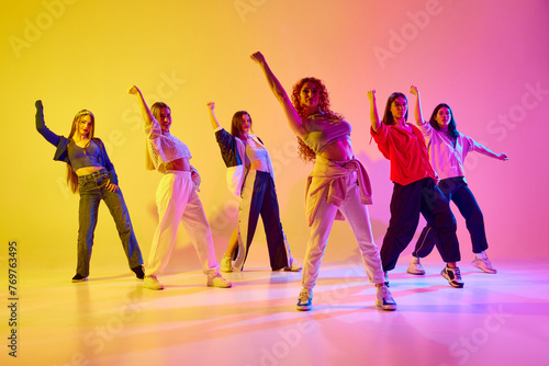 Fototapeta Naklejka Na Ścianę i Meble -  Talent show. Young women, group of artistic female dancers, woman performing streetstyle dance against gradient background in neon. Concept of youth, street dance, contemporary dance, modern, dynamics