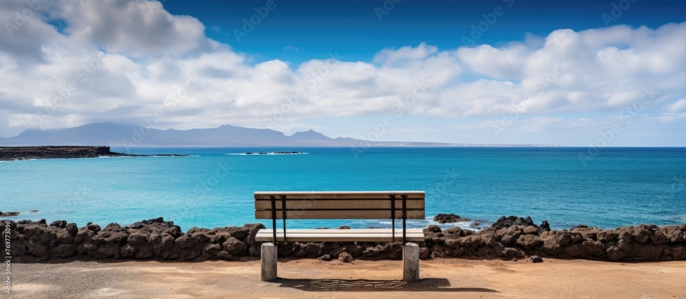 Enjoy the view of the ocean from a bench on the beach, surrounded by water, sky, and clouds. Relax in this coastal natural landscape while traveling or enjoying leisure time outdoors