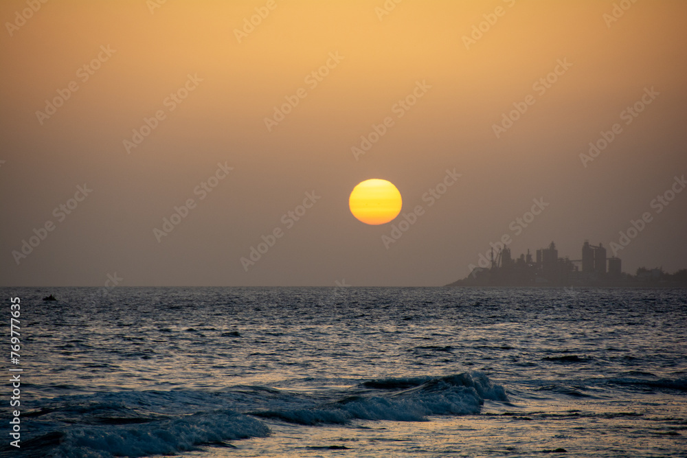 Sunset over the sea with a city in silhouette