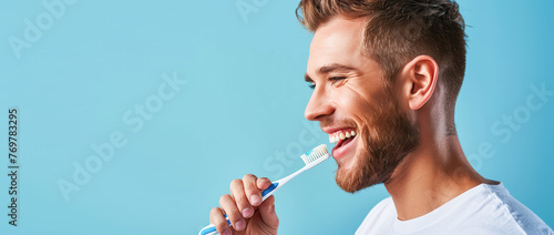 Portrait of a young man in profile who brushes his teeth with a manual toothbrush, blue background copy space. Concept of dental care and health, oral hygiene, prevention of dental diseases