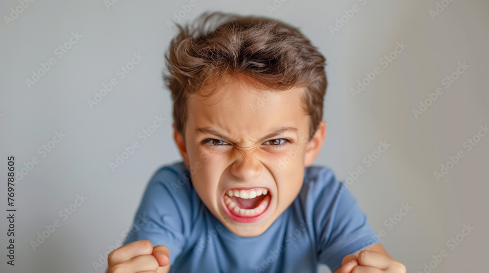 Angry little boy, screaming and shouting in blue tshirt on grey background Angry little boy, screaming and shouting in blue tshirt on grey background