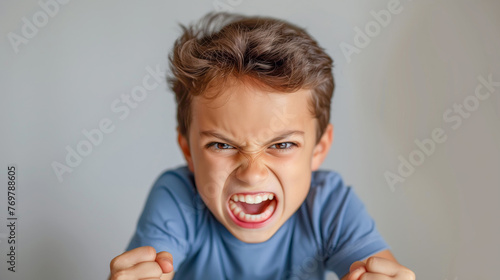 Angry little boy, screaming and shouting in blue tshirt on grey background photo