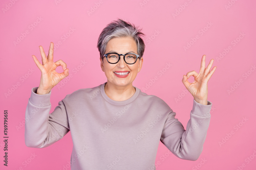 Photo of positive glad retired woman wear trendy jumper two hands demonstrate okey sign nice feedback isolated on pink color background Photo of positive glad retired woman wear trendy jumper two hands demonstrate okey sign nice feedback isolated on pink color background