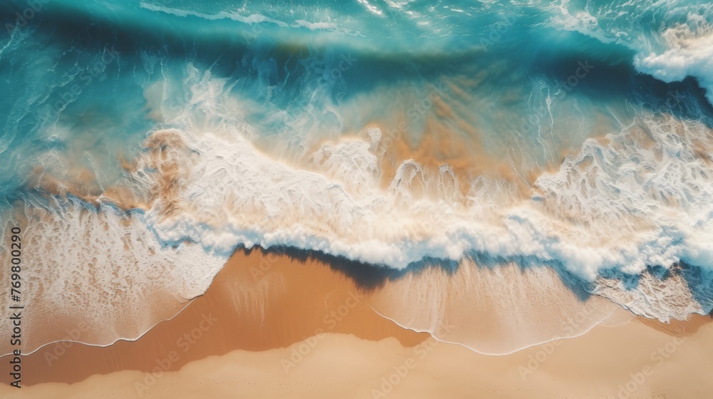 Aerial view of the ocean waves crashing against brown sand, creating dynamic patterns and textures.
