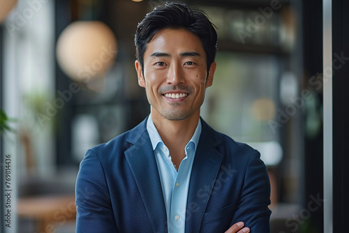 Portrait of a Confident Young Japanese Businessman Standing in Office in a Blue Business Suit. Successful Corporate Manager Posing for Camera with Crossed Arms, Smiling Cheerfully