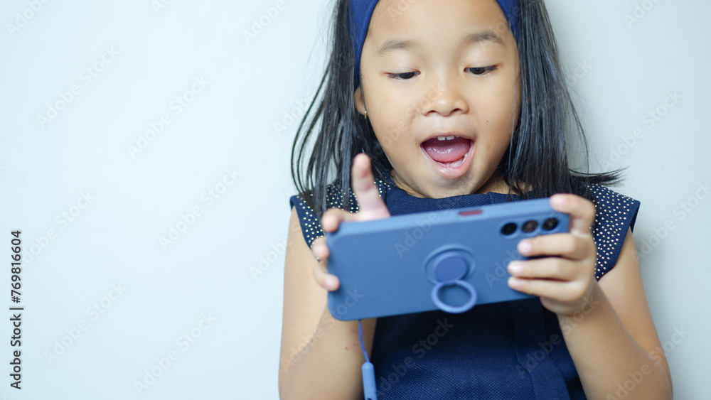 Portrait of happy little girl holding mobile phone, playing game standing isolated on white background. Technology concep Portrait of happy little girl holding mobile phone, playing game standing isolated on white background. Technology concep