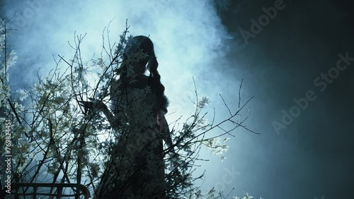 dark silhouette ghost fantasy woman goes to bright neon blue moon light ray in black night forest glow fog tree flowers. Mystery sexy lady Gothic fairy elf Girl fashion model. magic smoke mist art 4k