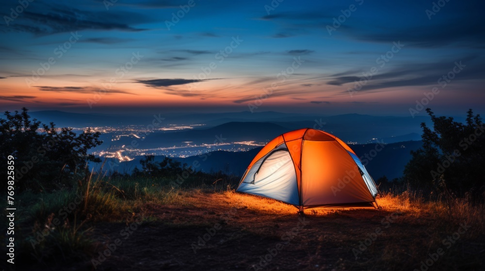 Camping tent illuminated by the glow of its lantern, set on top of an open grassy hill
