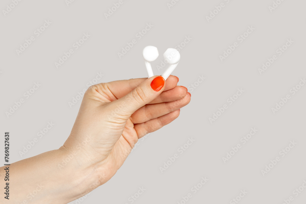 Closeup of woman hand showing white earphones for listening music, digital device. Indoor studio shot isolated on gray background. Closeup of woman hand showing white earphones for listening music, digital device. Indoor studio shot isolated on gray background.