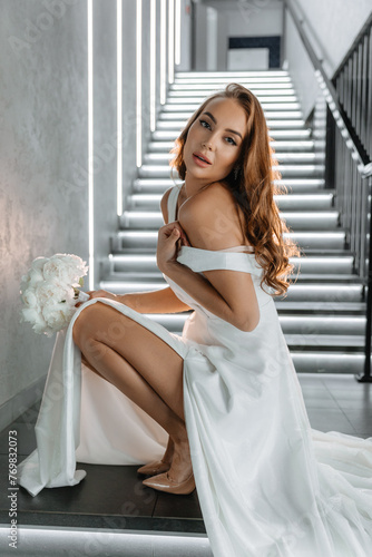 Portrait of a beautiful bride in a luxury dress with a bouquet of white peonies on the background of a restaurant
