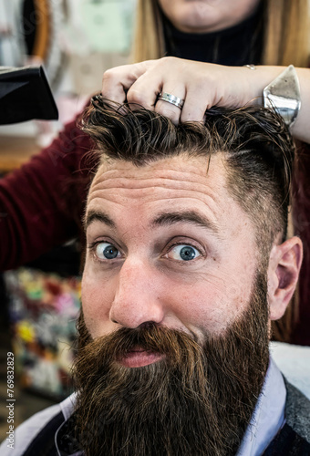 Hipster man getting stylish haircut at barber shop. Female hands of a hairdresser shaping a thick beard, a detailed scene of men's grooming.
