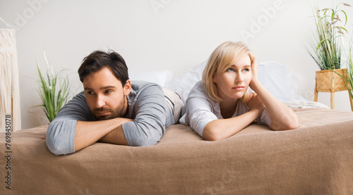 Unhappy sad couple, bearded man, blond woman, husband and wife lay on the bed, turned away from each other. Unlove crisis, sexual problem issues, relationship crisis, divorce  conflict - concept image